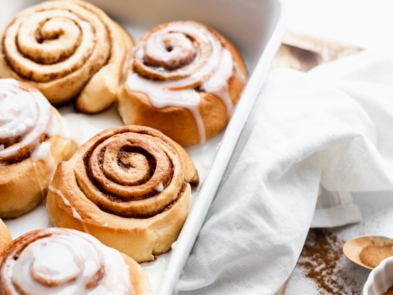 Cookie sheet of glazed cinnamon rolls with cinnamon on the side