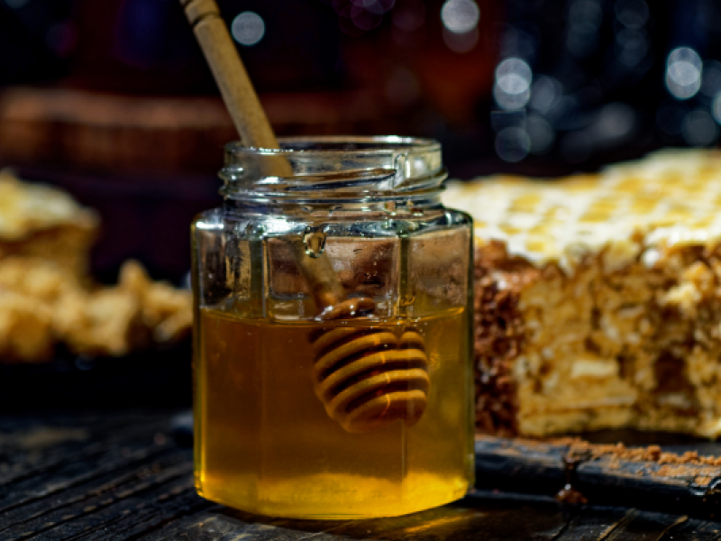 Stock image of jar of honey with honey spoon in foreground and honey cake in background