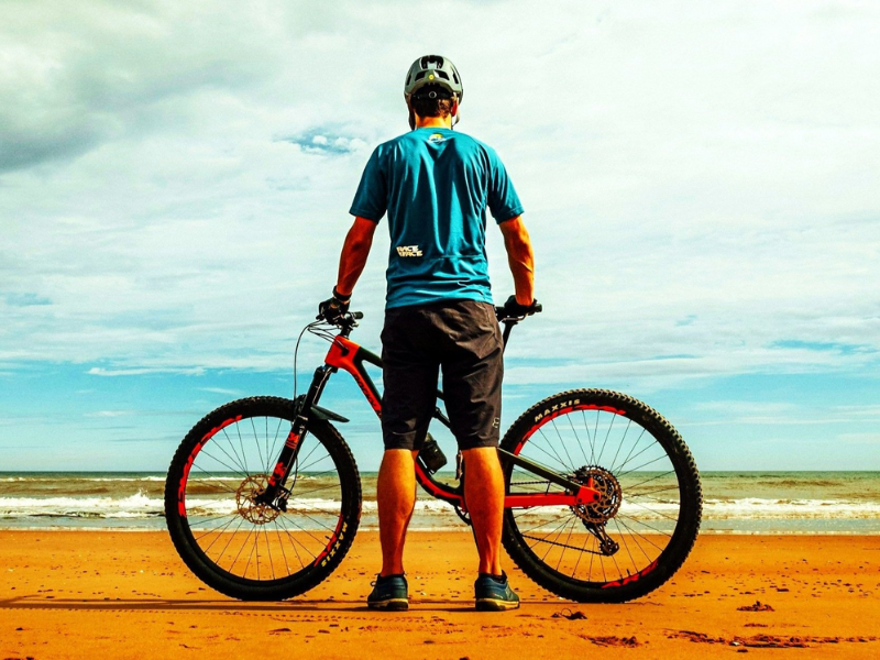 Cyclist with bike on beach facing the ocean