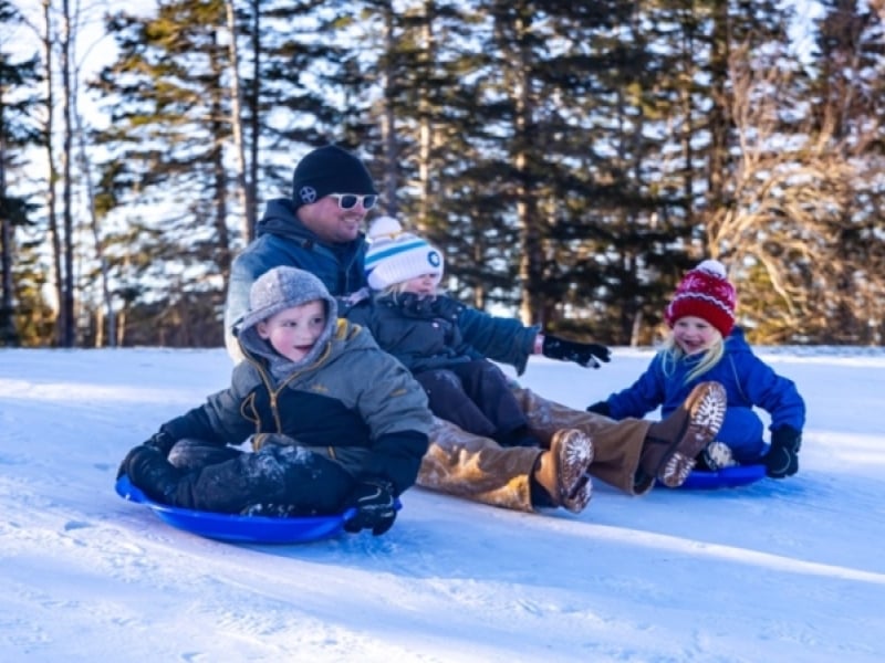 Adult and three children slide down snow-covered hill