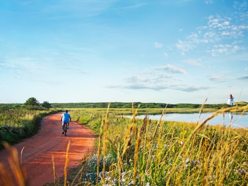 Lone cyclist on red dirt road to St. Peters Lighthouse in summer