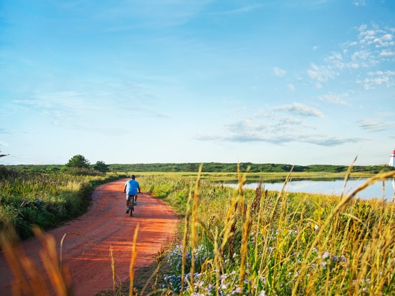 Lone cyclist on red dirt road to St. Peters Lighthouse in summer