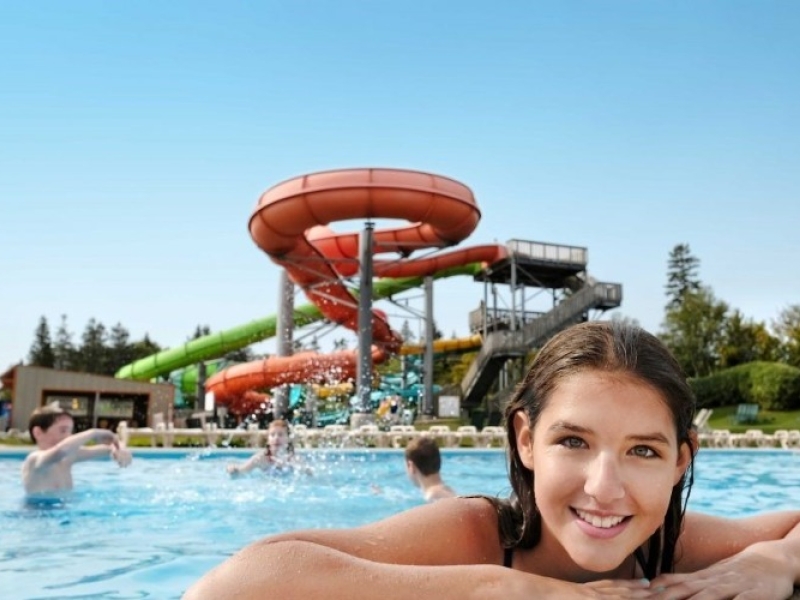 Young girl smiles on edge of pool with waterslides in background