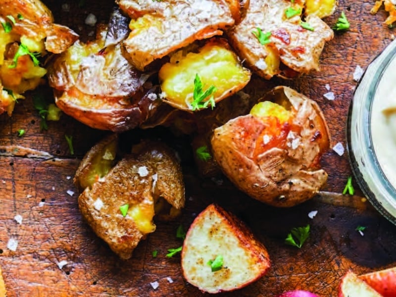 Smashed Crispy Baby Potatoes on wooden table with slight view of bowl of dip