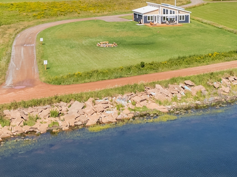 an Airele view of a grey cottage set on a rocky shore.