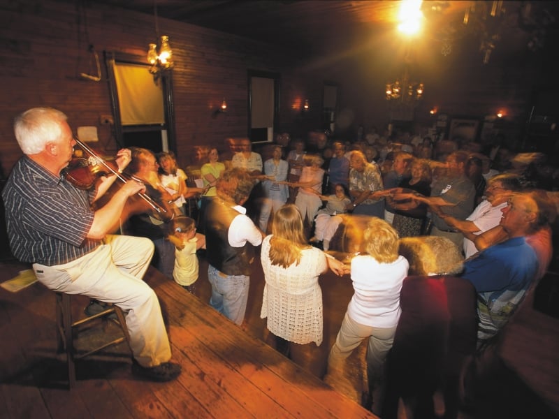 Fiddler in foreground with people doing square dance at Orwell Corner