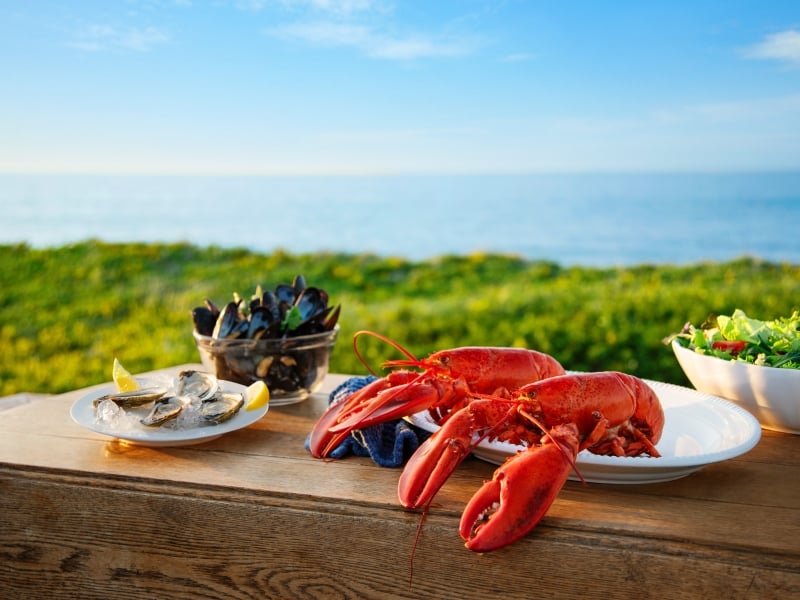 Plated PEI seafood and salad on a table with beach in background