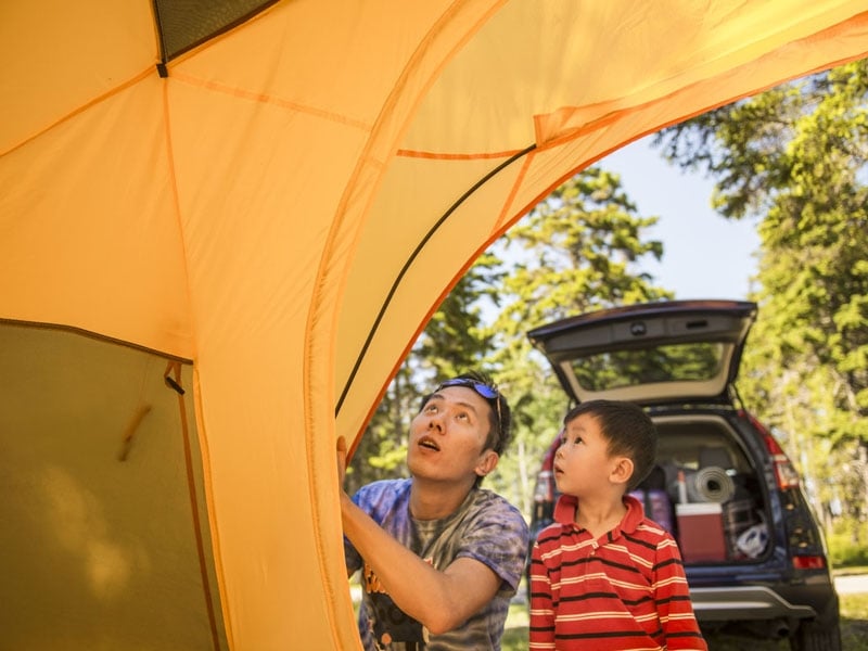 A man and child put up a small yellow tent in a wooded campsite in the PEI National Park