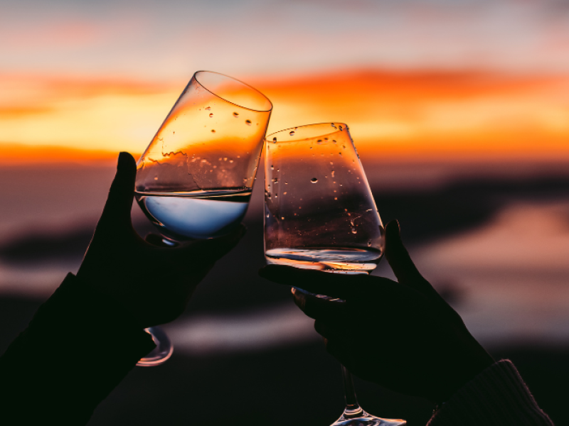 Stock image of couple holding wine glasses together with sunset in background; Source:Canva 