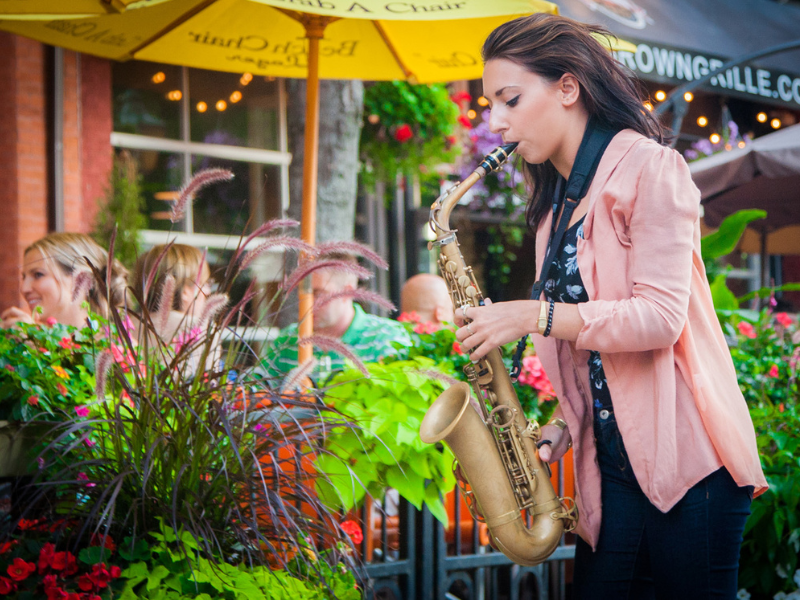 Musician plays saxophone on Victoria Row with patio diners in background