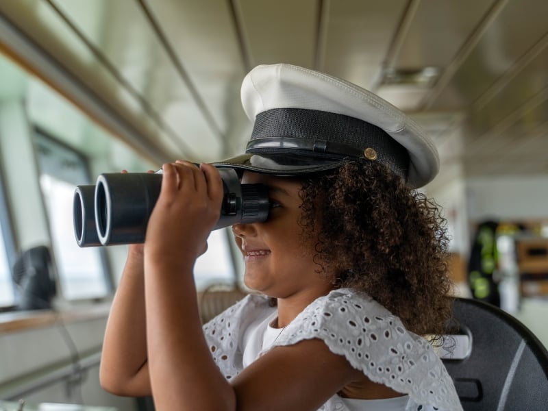 Young girl sports ferry captain hat and looks through binoculars