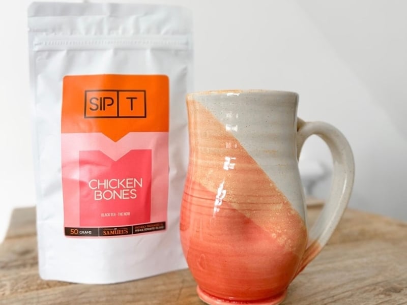 Pink and orange pottery mug sits next to package of Chicken Bones tea by SipT