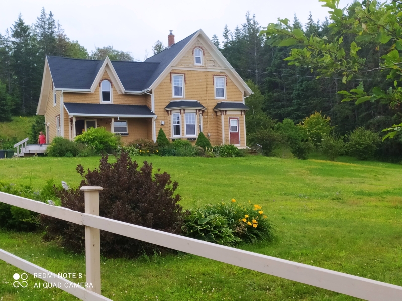 photo of the front view of Clinton Red Hills Summer House. Yellow house with gables and black roof