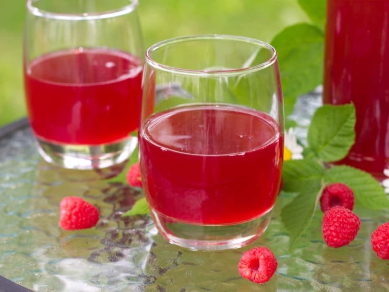 CLoseup of raspberry cordial served in tumblers with fresh raspberries and daisies on table