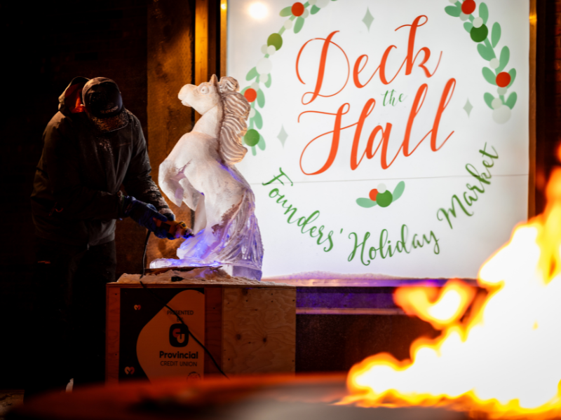 Live ice carving of a horse with illuminated Deck the Hall sign in background