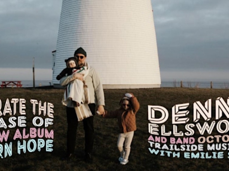 Photo of Dennis ellsworth holding a baby and the hand of a small child in front of a lighthouse