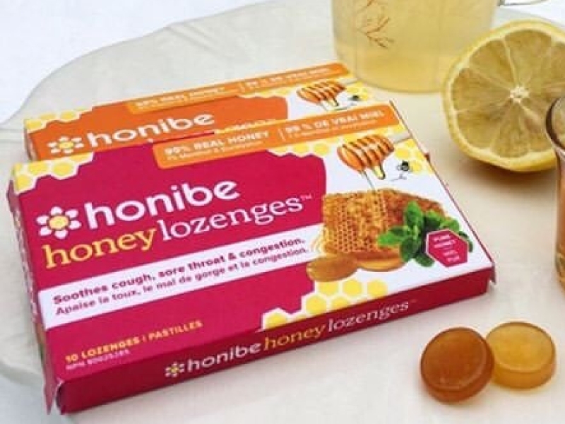 Package of Honibe lozenges sitting next to lemon and glass of lemon water
