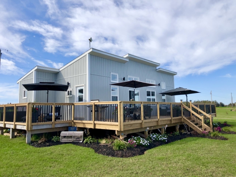 large grey cottage surrounded by a deck with umbrella seating areas.