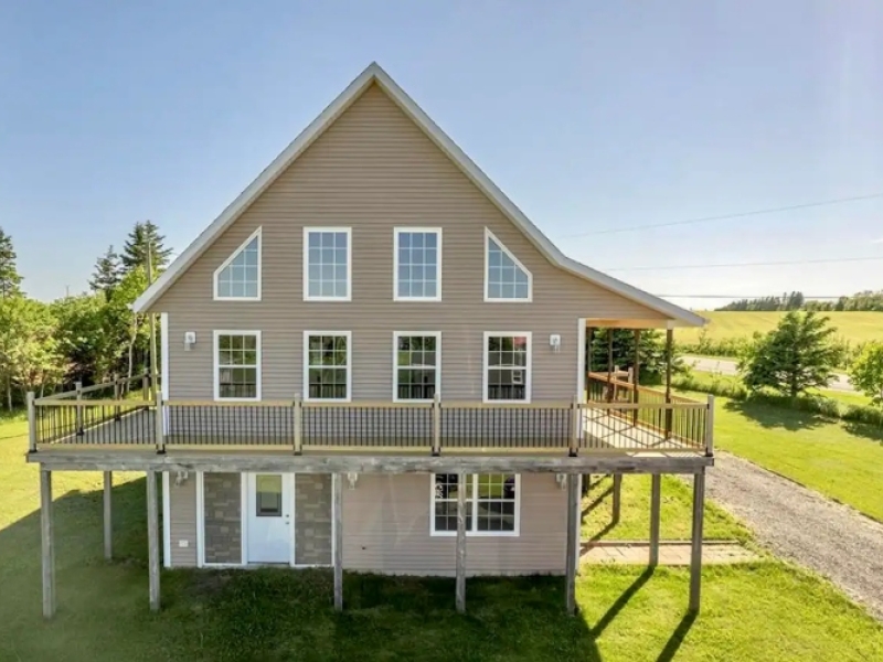 Photo of the front of two story beige home with many windows and wrap around deck.
