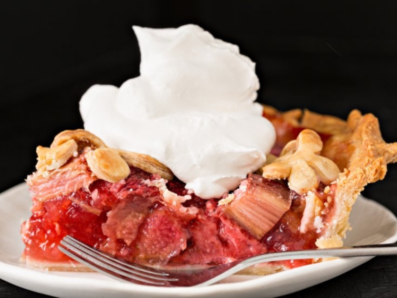 Piece of stawberry rhubarb pie with dollop of whipper cream plated with fork