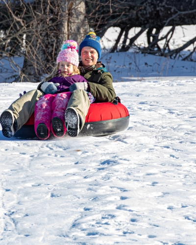 Parent and child in tube sliding down hill at Brookvale Nordic Park