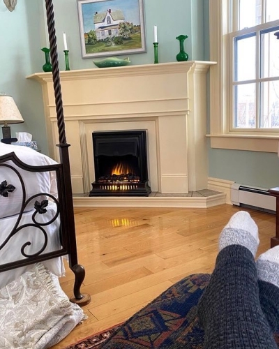 Interior inn guest room with guest's feet in cozy socks in foreground and poster bed and fireplace in background