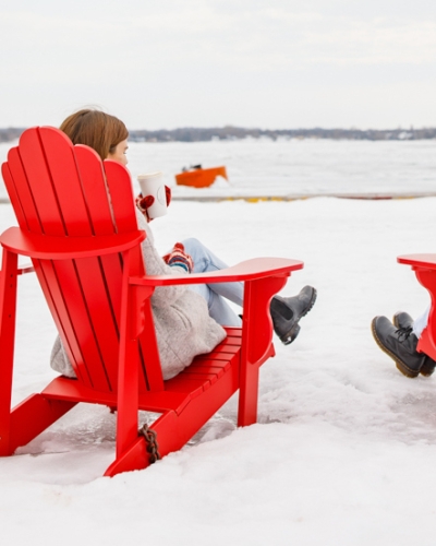 Two people sit in red adirondak chairs overlooking Charlottetown Harbour in winter