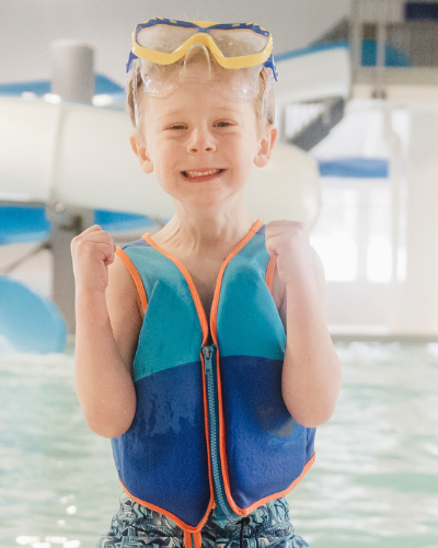 Close up of small boy on indoor pool deck with waterslide in background