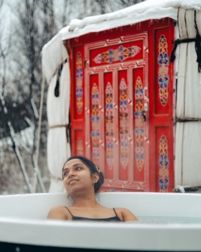 Woman in outdoor hot tub with yurt in background in winter