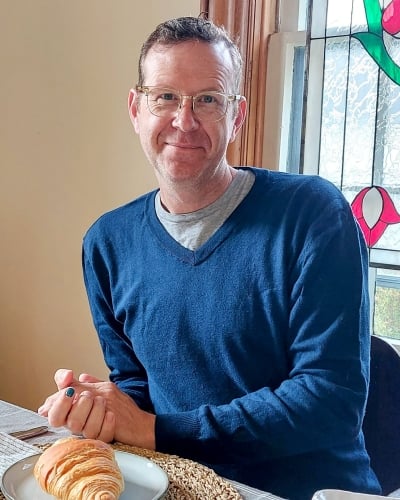 Image of Rod Weatherbie sitting at a dining room table with a crossaint on a plate