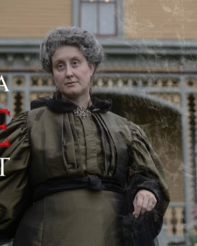 Fictitious spirit-medium Madame Evangeline Gray stands in front of Beaconsfield Historic House with title "Victorian-Era Séance Reenactment" 