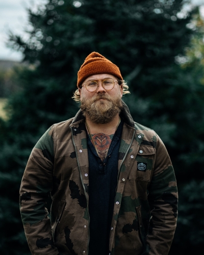 Portrait image of Al Douglas standing in front of an evergreen