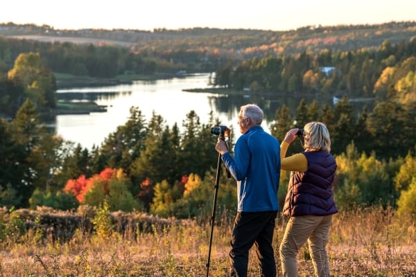 Couple birdwatching in fall in field overlooking Trout River