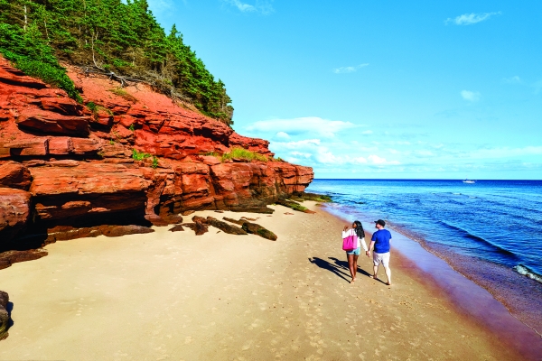 Couple walk on white sand beach at Red Point with red cliffs above