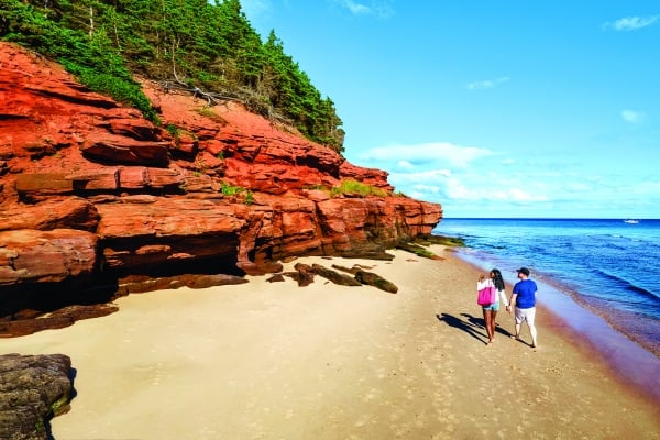 Couple walk on white sand beach at Red Point with red cliffs above