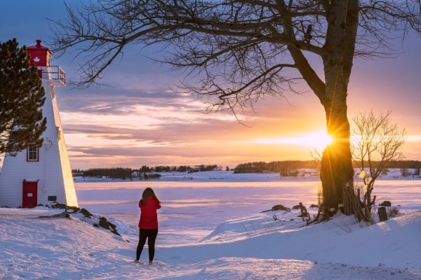 Female in red jacket next to Victoria Park Light looking over Charlottetown at sunset in winter