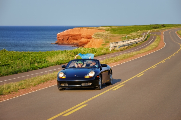 Couple driving convertible with top down along coastal drive