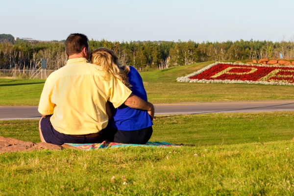 Couple sitting on grass in Borden-Carleton with PEI flower bed in distance
