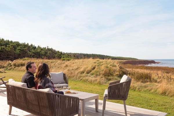 Couple sit on deck overlooking coastal view of red cliffs and water