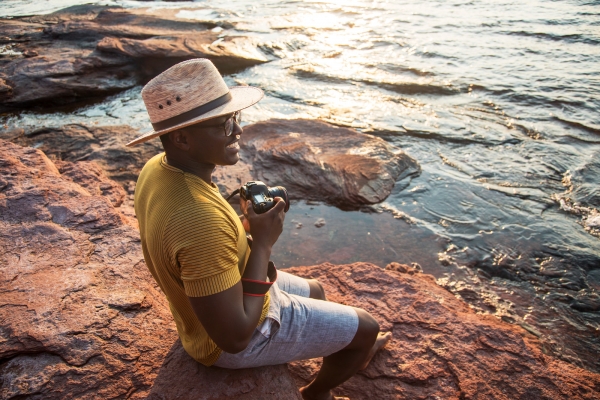 Man sits on rocks holding camera at PEI National Park, Cavendish
