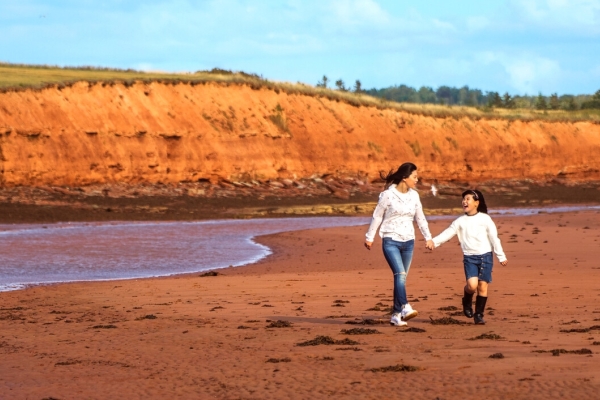 Adult and child walk along the sand with red cliffs in background at Argyle Shore Provincial Park