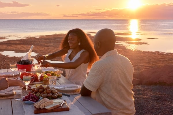 Group sits at picnic table at the beach at sunset for a dinner feast