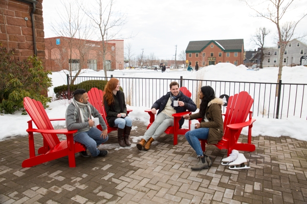 Group of four enjoying coffee in redchairs outdoors near Founder's Hall skating rink