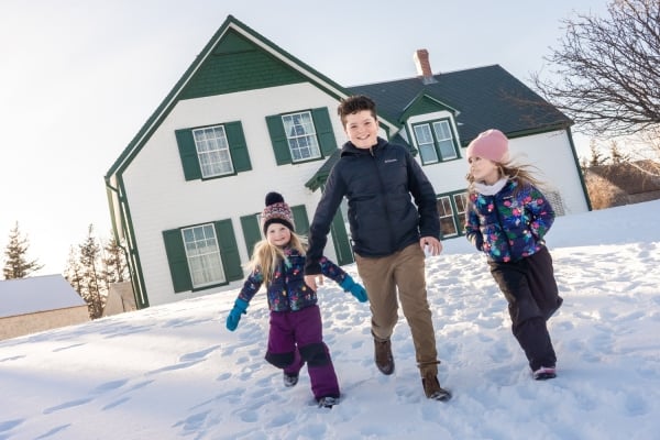 Three children run down hill in front of Green Gables Heritage Place in winter