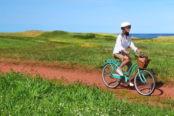 Woman on bicycle on red dirt lane to PEI beach under clear blue sky