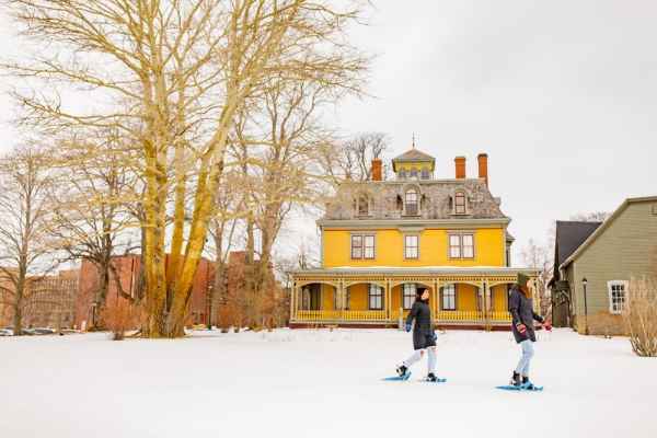 Two people snowshoe across front lawn at Beaconsfield Historic House in winter