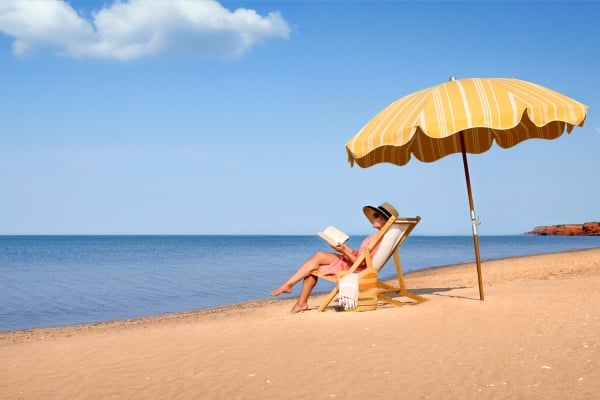 Women sitting in beach chair under umbrella reading a book on north shore beach, PEI