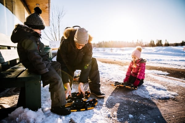 Male helps children put on snow shoes