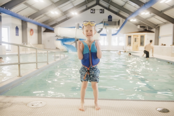 Young boy stands poolside with indoor waterslide in background