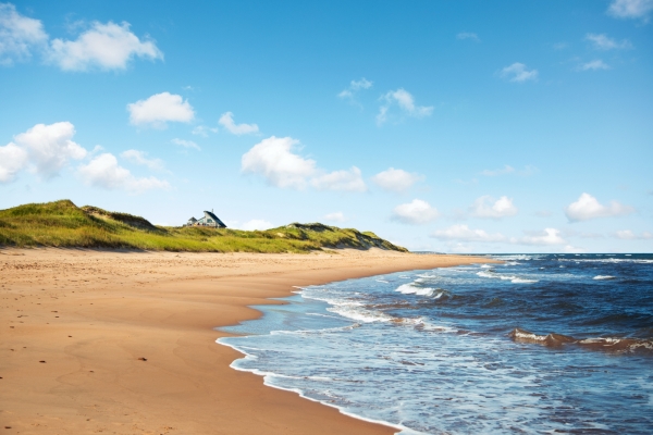 PEI white sand beach and sand dune under blue sky with cottage in distance